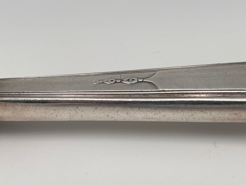 May include: Close-up of the handle of a silver fork with a decorative design.