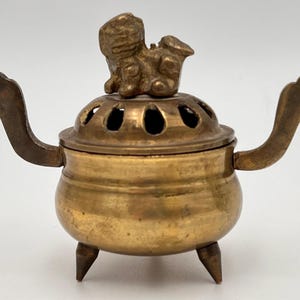 May include: A small brass incense burner with a lion finial and three legs. The burner has a perforated lid and two handles.