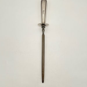 May include: A silver knife sharpener with a decorative handle and a round base. The sharpener is made of metal and has a long, thin blade.