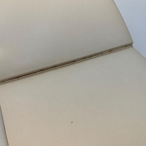 Puede incluir: Un cuaderno blanco cerrado, en blanco, con encuadernaci&oacute;n cosida.