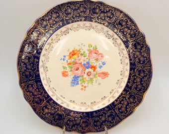 May include: A vintage dinner plate with a gold and blue rim and a floral design in the center. The plate has a scalloped edge and is in excellent condition.