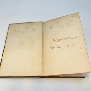 Puede incluir: Un libro abierto con p&aacute;ginas amarillentas y una inscripci&oacute;n manuscrita que dice "Maggie & Herbert Navidad 1899."