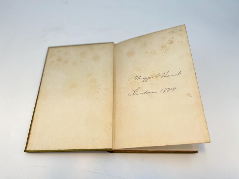Puede incluir: Un libro abierto con p&aacute;ginas amarillentas y una inscripci&oacute;n manuscrita que dice "Maggie & Herbert Navidad 1899."