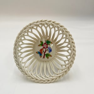 May include: A white porcelain basket with a woven design. The basket has a floral design in the center with red, blue, green, and yellow flowers.
