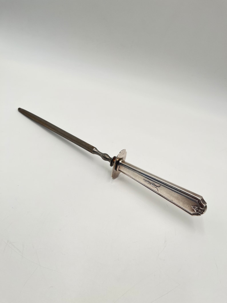 May include: A silver-plated steel skewer with a twisted handle. The handle has a decorative design and a small, round, flat base.