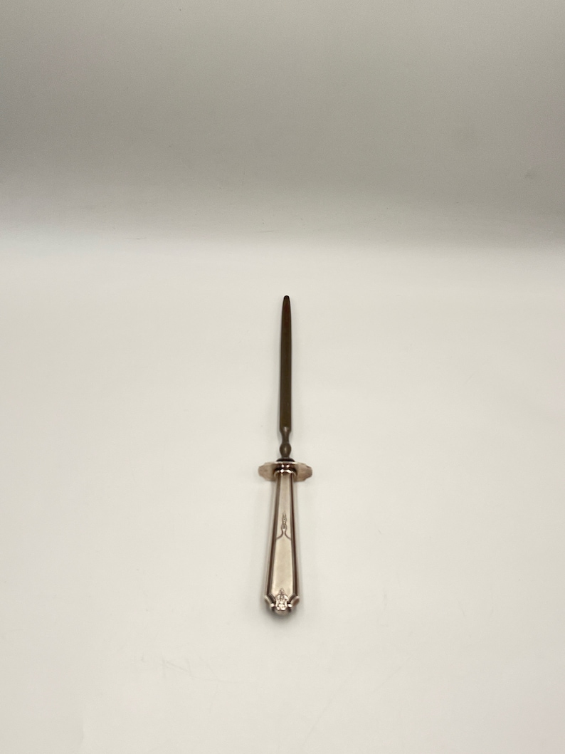 May include: A silver-plated skewer with a long, thin, pointed blade and a decorative handle.