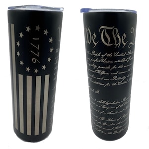 May include: Two black stainless steel tumblers with a silver design. One tumbler features the text "We The People" and the preamble to the United States Constitution. The other tumbler features a silver American flag with 13 stripes and 13 stars in a circle with the year 1776.