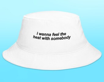 May include: White bucket hat with the text "i wanna feel the heat with somebody" embroidered in black.