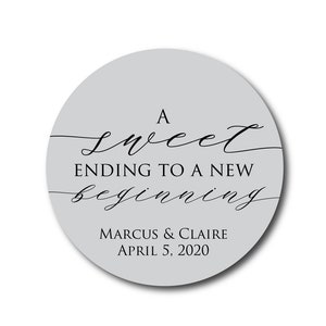 May include: A round, gray sticker with the text "A sweet ending to a new beginning" in black cursive font. Below the text is "Marcus & Claire April 5, 2020" in black sans-serif font.
