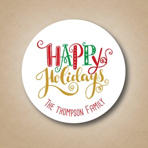 Pode incluir: Etiqueta redonda branca com o texto "Boas Festas" em letras vermelhas, verdes e douradas. O texto "The Thompson Family" est&aacute; impresso em preto abaixo da sauda&ccedil;&atilde;o.
