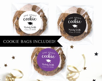May include: Three clear plastic bags with brown chocolate chip cookies inside. Each cookie has a round sticker with the text "one smart cookie" and a graduation cap graphic. The text "Melody Smith Class of 2028" is on each sticker. The stickers are white with black text on one bag, black with white text on another bag, and purple with white text on the third bag. The bags are on a white surface with gold and black confetti.