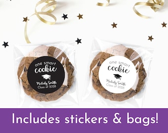 May include: Two clear plastic bags with brown cookies inside. Each cookie has a round black and white sticker that says "one smart cookie" with a graduation cap icon and the text "Melody Smith Class of 2028". The text "Includes stickers & bags!" is at the bottom of the image.