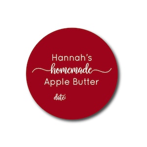 May include: A round, deep red label with the text "Hannah's homemade Apple Butter" in white script. The word "homemade" is in cursive. Below the text is the word "date:" in a smaller font.