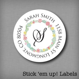 Könnte beinhalten: Ein weißer runder Aufkleber mit einem floralen Kranzdesign. Der Kranz besteht aus rosa, gelben, blauen und grünen Blumen. In der Mitte des Kranzes befindet sich ein schwarzer Buchstabe "S". Der Text "SARAH SMITH 1158 MAIN ST LONGMONT CO 80504" ist um den Kranz herum gedruckt.