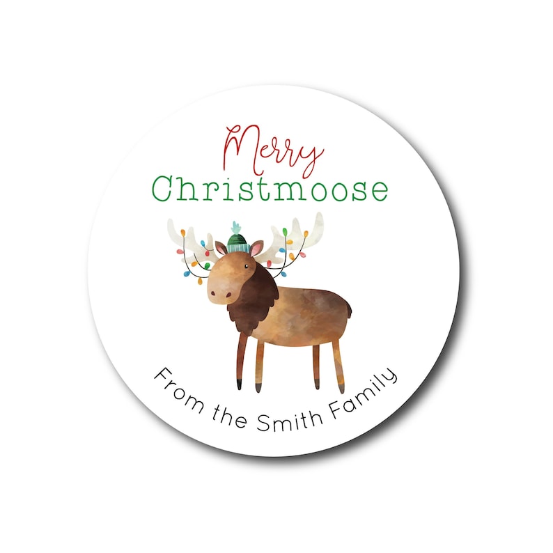 Op de afbeelding: Een ronde witte sticker met een groene en bruine cartoon-elch die een groene en blauwe hoed draagt met lichtjes rond zijn gewei. De tekst "Merry Christmoose" is in groen en rood en de tekst "From the Smith Family" is in groen.