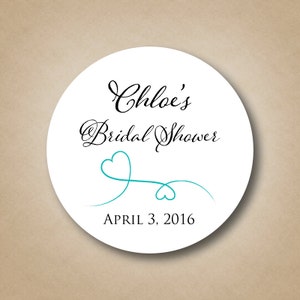 May include: White round sticker with black text that reads "Chloe's Bridal Shower" and "April 3, 2016". A teal blue heart design with a swirl is below the text.