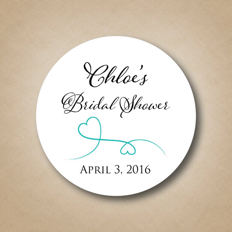 May include: White round sticker with black text that reads "Chloe's Bridal Shower" and "April 3, 2016". A teal blue heart design with a swirl is below the text.