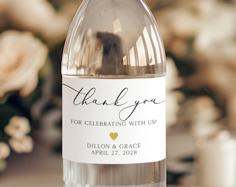 May include: White wedding favour water bottle label with black calligraphy text that says "Thank you for celebrating with us!" with a gold heart and the names Dillon & Grace and the date April 27, 2028.