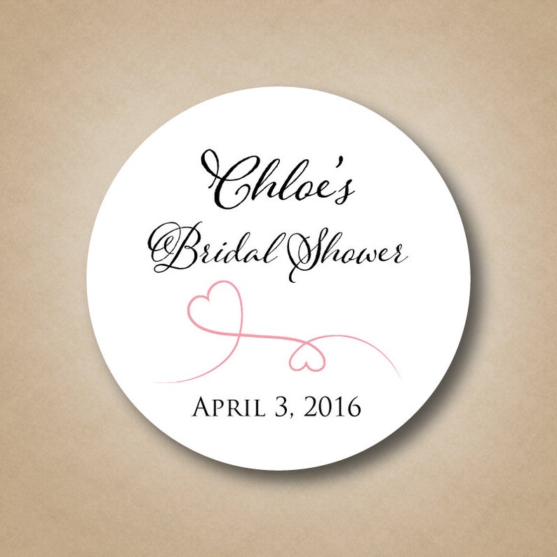 May include: White round sticker with black text that reads "Chloe's Bridal Shower" and "April 3, 2016". A pink heart design with a thin line is below the text.