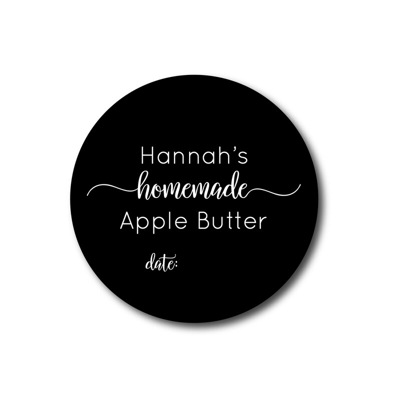 May include: A round, black label with white text. The label reads "Hannah's homemade Apple Butter" in a script font, with the word "homemade" in cursive. Below, the word "date:" is printed.