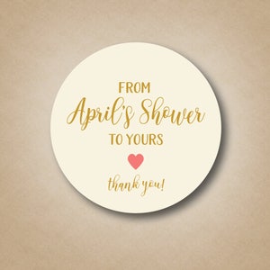 May include: Round white sticker with gold text that says "From April's Shower to Yours" with a pink heart and the words "thank you!"