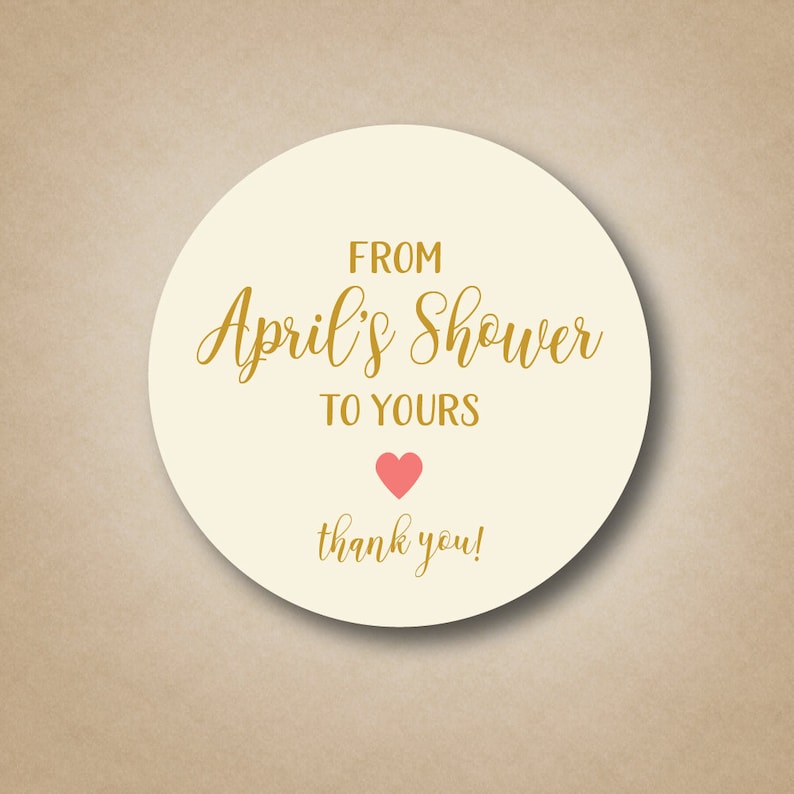 May include: Round white sticker with gold text that says "From April's Shower to Yours" with a pink heart and the words "thank you!"