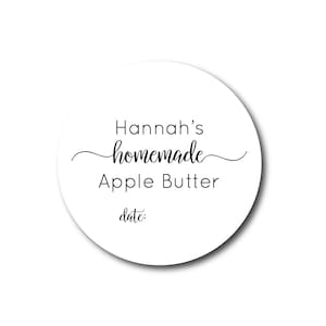 May include: A round white label with the text "Hannah's homemade Apple Butter date:" in black script and sans-serif fonts. The word "homemade" is in a cursive font. The label has a shadow.