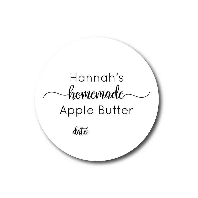 May include: A round white label with the text "Hannah's homemade Apple Butter date:" in black script and sans-serif fonts. The word "homemade" is in a cursive font. The label has a shadow.