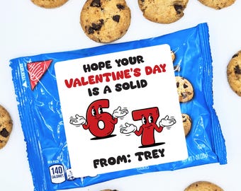 May include: A blue cookie bag with a white label featuring the text "HOPE YOUR VALENTINE'S DAY IS A SOLID 67 FROM: TREY." The label has red cartoon numbers. Chocolate chip cookies surround the bag. The bag contains 1 oz (28g) of cookies.