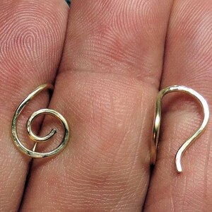 May include: A pair of gold-colored spiral earrings. One earring features a complete spiral design, while the other has a curved hook. The earrings are shown against a skin-toned background.