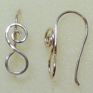 May include: A pair of silver-toned earrings. Each earring features a spiral design at the top and a curved hook for the ear. The earrings are displayed against a light yellow background.