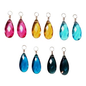May include: A collection of ten teardrop-shaped faceted glass pendants arranged in two rows. Each pendant features a silver-toned wire loop at the top. The colors include shades of pink, yellow, light blue, medium blue, and dark blue.