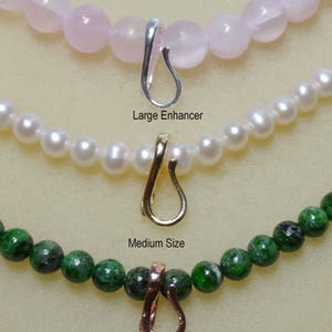 May include: Three necklaces with different beads and enhancer clasps. The top necklace has pink beads with a silver enhancer. The middle necklace has white pearls with a gold enhancer. The bottom necklace has green beads with a copper enhancer. The text reads "Large Enhancer" and "Medium Size".