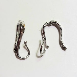 Könnte beinhalten: Zwei silberfarbene Metallverschlüsse, wahrscheinlich für Schmuck oder Accessoires, werden vor weißem Hintergrund gezeigt. Die Verschlüsse haben ein gebogenes Design mit Haken- und Ösenverschluss. Das Metall hat eine glänzende, reflektierende Oberfläche.