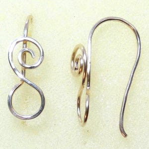 Peut inclure: Une paire de boucles d'oreilles en métal argenté au design en fil continu. Chaque boucle d'oreille se compose d'une boucle circulaire à la base qui se transforme en une forme en spirale, s'étendant vers le haut en un crochet incurvé.