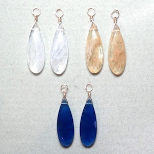May include: Six teardrop-shaped pendants arranged in three pairs. The top left pair is clear, the top right pair is a mottled peach color, and the bottom pair is a deep blue. Each pendant features a wire-wrapped metal loop at the top for hanging.