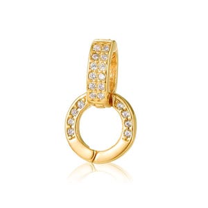 May include: A gold-toned circular pendant featuring a hinged bail, both adorned with small, clear, sparkling stones. The design consists of a round ring suspended from a rectangular, stone-encrusted connector, creating a cohesive jewelry piece.