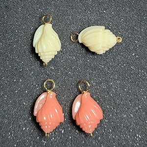 May include: Four shell-shaped charms featuring carved details and gold-tone metal jump rings. Two charms are cream-colored, and two are coral-pink. Each charm has a smooth, polished finish with a spiral design, designed for jewelry making projects.