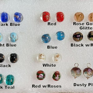 May include: A collection of round glass beads arranged in pairs, labeled by color and pattern: Dark Blue, Light Blue, Black, Dark Teal, Red, Blue, White, Red w/Roses, Rose Gold Glitter, Black w/Roses, and Dusty Plum with gold metal loops.