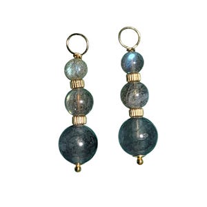 May include: A pair of drop earrings featuring three graduated round grey beads with a marbled texture, separated by small gold-toned cylindrical spacers. Each earring is topped with a gold-toned circular hoop and finished with a small gold-toned bead at the base.