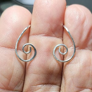 May include: A pair of silver-colored spiral earrings. Each earring features a curved, elongated design that culminates in a tightly wound spiral. The earrings are displayed against a blurred background.