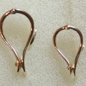 May include: Two teardrop-shaped jewelry clasps. The clasps are made of a combination of rose gold and silver-colored metal. The clasps are designed with a loop at the top and a pointed end, and are set against a light background.
