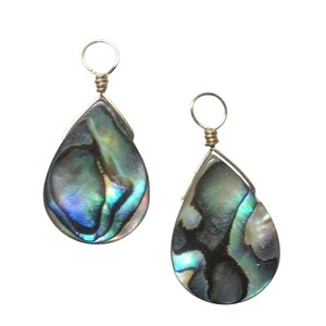 May include: Two teardrop-shaped pendants made of iridescent abalone shell with swirling patterns of dark blue, green, and purple. Each pendant features a silver-toned metal wire bail at the top, designed for attachment to a necklace or earring hook.
