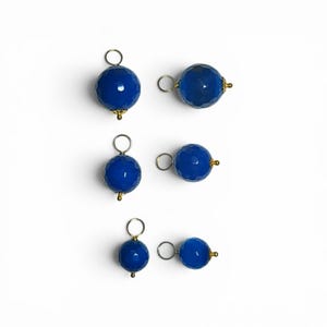 May include: Six spherical blue charms with a faceted surface texture. Each charm features a small silver-toned jump ring at the top and a decorative gold-toned metal cap at the base, arranged in three pairs of varying sizes on a white background.