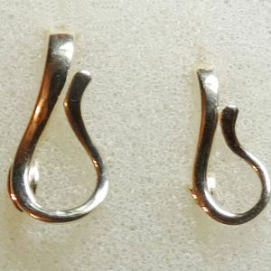May include: Two silver-colored, teardrop-shaped earring hooks. The hooks have a curved design with a loop at the bottom and a straight top. The earrings are displayed on a textured, off-white surface.