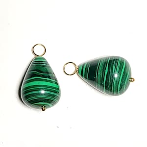 May include: Two teardrop-shaped malachite pendants featuring distinct dark and light green banded patterns. Each polished stone is capped with a small gold-toned metal jump ring at the top, providing a secure loop for attachment to jewelry chains.