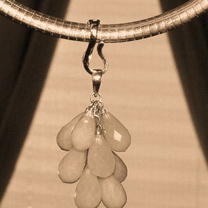 May include: A sepia-toned image of a necklace featuring a gold-colored chain and pendant. The pendant is a cluster of pale peach-colored, teardrop-shaped gemstones. The necklace is suspended against a neutral background.