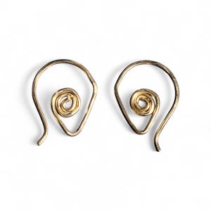 Puede incluir: Un par de pendientes en espiral de color dorado. Cada pendiente presenta un marco en forma de lágrima con un diseño en espiral enrollada en el centro. Los pendientes se muestran sobre un fondo blanco.