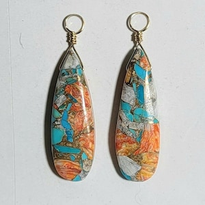May include: Pair of teardrop-shaped earrings with a gold wire loop. The earrings feature a mosaic of turquoise, orange, gold, and white stones. The stones are arranged in a teardrop shape, with a gold wire wrapped around the top.