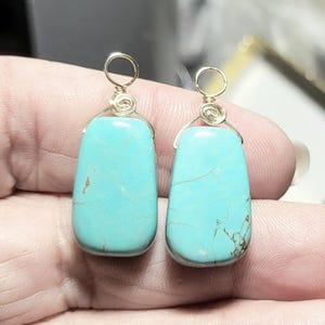 Puede incluir: Un par de pendientes de piedra turquesa con detalles de alambre dorado. Las piedras en forma de lágrima tienen vetas naturales y están suspendidas de un lazo simple. Estos pendientes son un accesorio único.